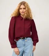 Camisa celeste de crepé con cuello inglés, manga larga abullonada y abotonadura frontal.