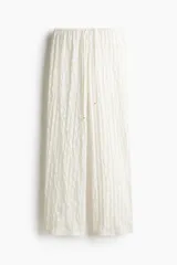 Pantalón blanco de corte holgado con tejido calado tipo encaje, tiro bajo, piernas extralargas, elástico en la cintura y cordón para ajustar.