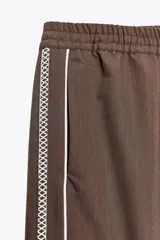 Pantalón de tiro alto negro a rayas verticales blancas, con cintura elástica ajustable con cordones, bolsillos delanteros y banda lateral blanca.