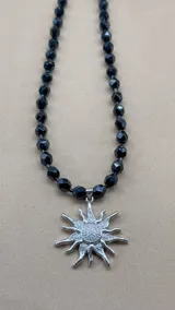 Collar corto de cuentas facetadas negras con dije de sol plateado con circonitas.