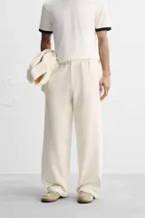 Pantalón color crema de corte amplio, con cintura elástica ajustable con cordón, bolsillos laterales y trasero, cierre frontal con cremallera y botón.