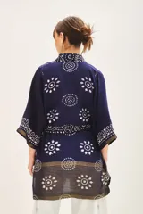 Saco tipo kimono de manga larga, color azul marino con estampado batik o blockprint en blanco y detalles en dorado/bronce en los bordes. Posee solapas anchas y lazo para ajustar a la cintura.