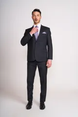 Traje de vestir de hombre color gris oscuro, compuesto por saco de dos botones con solapa de muesca, bolsillo de ojal en el pecho y bolsillos con solapa en los laterales, y pantalón de corte recto. Incluye camisa blanca, corbata lila y pañuelo de bolsillo lila.