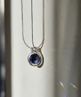 Collar plateado con dije redondo con piedra azul facetada.