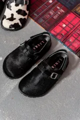 Zuecos negros con textura de pelo, hebilla plateada y suela plana.