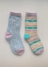 Pack de dos pares de medias de media caña con diseños diferentes: un par gris con lunares blancos y puntera y talón rosas, y otro par con rayas horizontales de colores y puntera y talón rosas.