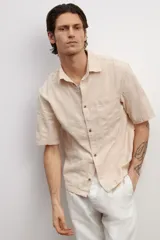 Camisa de manga corta color rosa claro, con cuello inglés, tapeta lisa, bolsillo superior abierto, canesú en la espalda y bajo recto.
