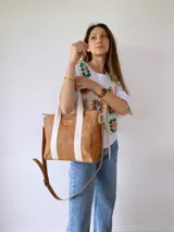 Bolso tipo tote de cuero color camel con dos tiras verticales blancas y correa larga ajustable al hombro.