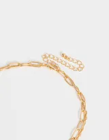 Collar corto dorado de doble cadena, una de eslabones grandes y otra de eslabones finos, con dije de perla irregular y ángel dorado.