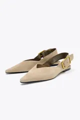 Zapato plano destalonado color beige, de serraje, con punta fina y tira trasera con hebilla metálica.