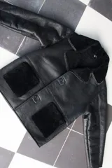 Gamulán negro de cuero genuino con cuello y solapas de piel sintética. Cierre frontal con botones y bolsillos de parche con ribete de piel sintética.