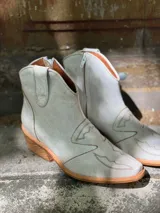 Botas cortas de cuero sintético color beige con detalles de costuras estilo western.