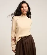 Blusa de punto color crema, con cuello alto y mangas largas.