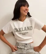 Blusa cropped de algodón color blanco, con cuello redondo, manga corta y estampa lettering "Oakland California 1995" en el frente.