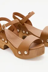 Sandalias con plataforma de madera, tira ancha de cuero color marrón claro en la parte delantera y pulsera al tobillo con hebilla.