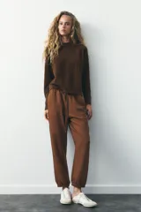 Pantalón jogger color gris claro, de tiro alto con cintura elástica ajustable con cordones, bolsillos delanteros y traseros con solapa, y puños elásticos en el bajo.
