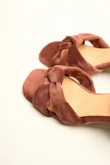 Sandalia de terciopelo verde con taco cuadrado de 7 cm, punta cuadrada y tiras anchas anudadas en el empeine. Cuenta con una tira fina ajustable al tobillo con hebilla dorada.