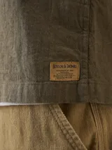 Camisa color verde militar de manga larga con cuello clásico, cierre frontal con botones y dos bolsillos de parche en el pecho.