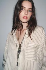 Set de dos collares largos de eslabones metálicos color peltre. Uno presenta un dije con flecos colgantes y abalorios de colores verde, blanco y negro. El otro es una cadena simple.