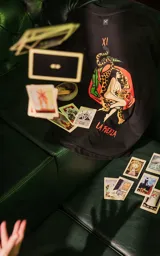 Remera negra de manga corta con cuello redondo y calce oversize. Presenta una estampa en la espalda inspirada en el tarot, con la carta "La Fuerza" que muestra a una mujer desnuda sobre un leopardo, rodeada de vegetación y un sol rojo.
