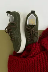 Zapatillas de gamuza color verde oliva con cordones marrones, pespuntes decorativos y suela de plataforma blanca.