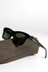 Lentes de sol negros con marco rectangular y lentes verdes.