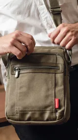 Morral color verde militar de tela canvas con detalles en símil cuero, correa de galón regulable y cierre superior. Tiene dos bolsillos frontales con cierre, bolsillo trasero con cierre y bolsillos internos.
