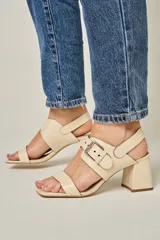 Sandalias de cuero color champagne, con punta cuadrada, tira ancha sobre el empeine y tira al tobillo con hebilla metálica. Taco cuadrado de 7 cm.