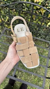 Sandalias bajas color marrón con tiras de cuero entretejidas y hebilla lateral.