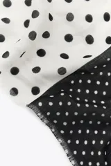 Pañuelo cuadrado con estampado de lunares blancos sobre fondo negro en la mitad superior y lunares negros sobre fondo gris en la mitad inferior.
