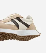 Championes de estilo jogging para mujer, confeccionados en poliuretano color tostado con recortes contrastantes en color crema. Presentan cierre de cordones blancos y suela de PVC que se extiende hasta el talón con base dentada.