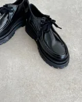 Mocasín negro tipo creeper, hecho de cuero vacuno, con suela gruesa y cómoda.