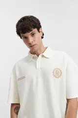 Remera polo color beige con textura acanalada, corte oversize, cuello clásico con botones y logo estampado en el pecho.