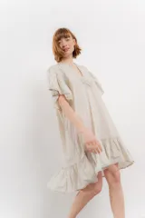 Vestido corto color beige confeccionado en algodón, con escote en V con detalles bordados, mangas cortas amplias con volados y falda con ruedo en volado.