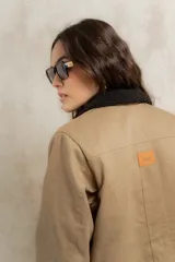Campera color beige con cuello de corderito negro, cierre con botones, bolsillos laterales y puños con detalle de cuero sintético negro.