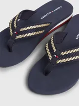 Ojotas Tommy Hilfiger color azul marino con tiras trenzadas en dorado y detalles distintivos de la marca.