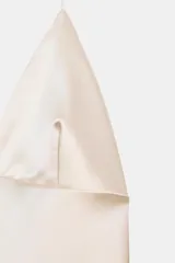 Vestido midi de seda color crema, con escote pronunciado en pico y tirantes finos ajustables tipo halter. El bajo es asimétrico y está adornado con un delicado encaje a tono.