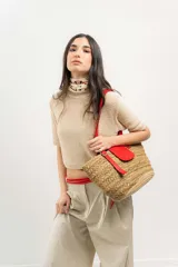 Bolso tipo canasto de paja con detalles en cuero rojo, incluyendo un bolsillo externo con solapa y cierre con botón a presión, y correa regulable.