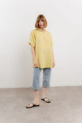 Camisa amarilla de lino con corte recto y calce suelto. Tiene cuello camisero, botones en el frente y mangas cortas con presilla y botón.