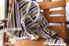 Blusa de tejido calado a rayas horizontales en tonos borgoña, amarillo, lila y blanco, con mangas largas acampanadas y terminación de volados con puntilla blanca.