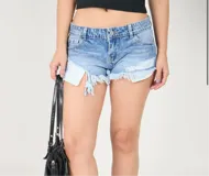 Short de jean celeste con efecto lavado, tiro bajo, corte irregular con roturas y terminación desflecada.