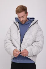 Campera puffer de hombre color gris claro, con capucha ajustable con cordón, cierre de cremallera frontal, bolsillos laterales y mangas largas. Tejido acolchado resistente al viento.