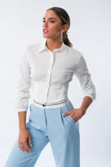 Camisa blanca de algodón y elastano, con corte cropped, cuello clásico, mangas largas con puños elásticos y cintura ajustada con elástico.