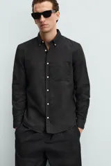 Camisa celeste a rayas verticales, de corte relaxed fit, confeccionada en lino y algodón. Tiene cuello abotonado, manga larga con puños abotonados, bolsillo de parche en el pecho y cierre frontal con botones.