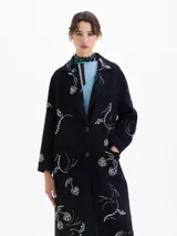 Tapado largo de paño color azul marino con bordados de piedras color cristal en forma de cerezas y pájaros. Posee cuello de solapa, cierre frontal con botones y bolsillos laterales.
