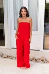 Conjunto de dos piezas color rojo vibrante, compuesto por un top strapless con diseño asimétrico superpuesto y un pantalón de tiro alto con pierna ancha y bolsillos laterales.