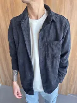 Sobrecamisa de pana negra con cuello clásico, cierre frontal con botones, manga larga con puños abotonados y bolsillo de parche en el pecho.
