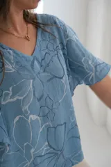 Blusa celeste con estampado de flores blancas y azules, de corte amplio y mangas cortas.