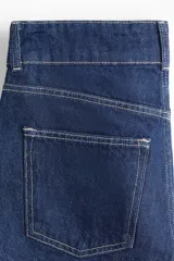 Short de jean azul oscuro, tiro alto, con cierre y doble botón metálico dorado. Presenta corte holgado y costuras visibles en hilo contrastante claro.