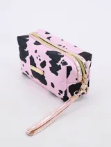 Neceser rectangular con estampado de manchas de vaca en tonos rosa y negro, cierre superior con cremallera dorada y correa de muñeca extraíble.